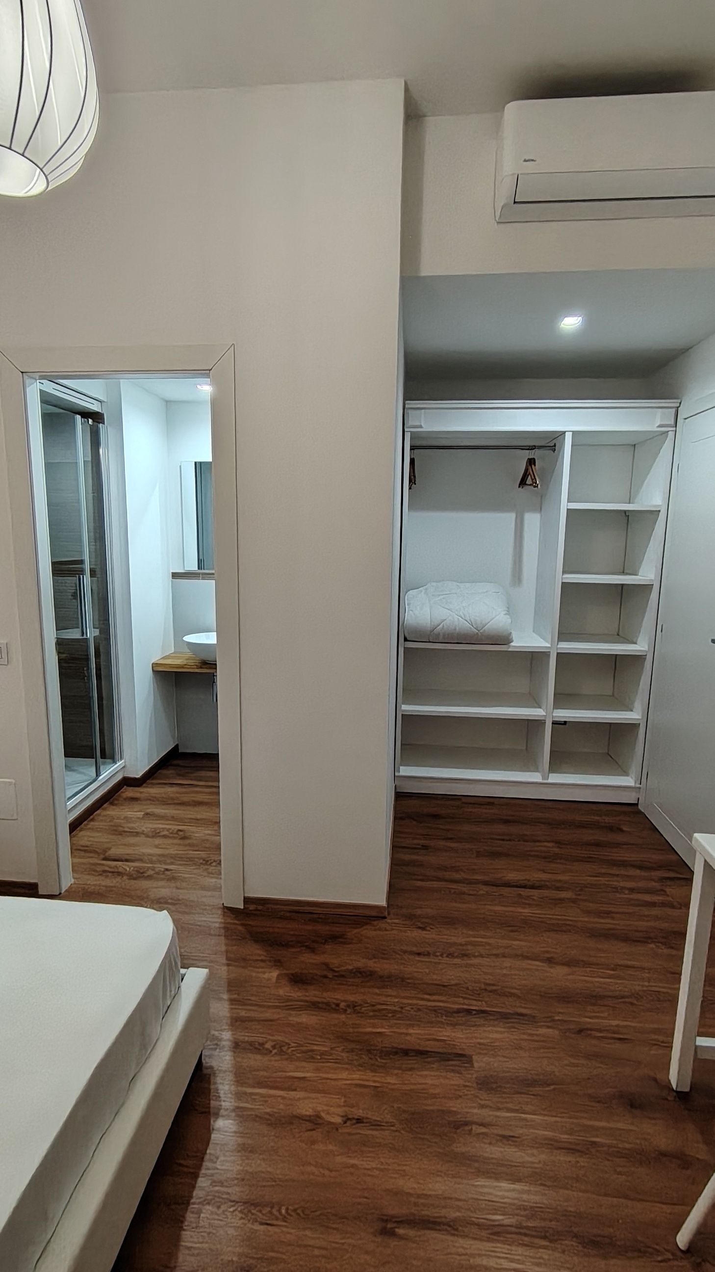 Ein Schlafzimmer mit Holzboden, einem Bett, einem Kleiderschrank und einer Klimaanlage.