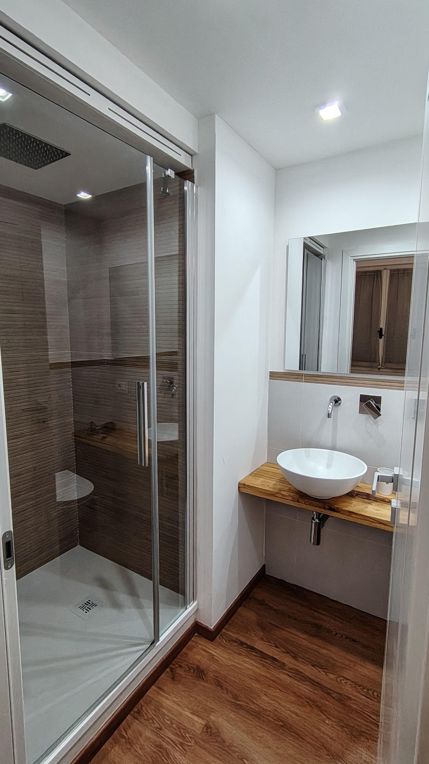 Ein modernes Badezimmer mit einer Duschkabine aus Glas, einem Holz-Waschtisch und einem weißen Waschbecken.