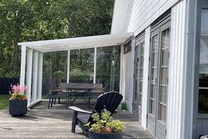Eine überdachte Terrasse im Freien mit Tisch, Stühlen, Blumentöpfen und einer Glastür zum Gebäude.