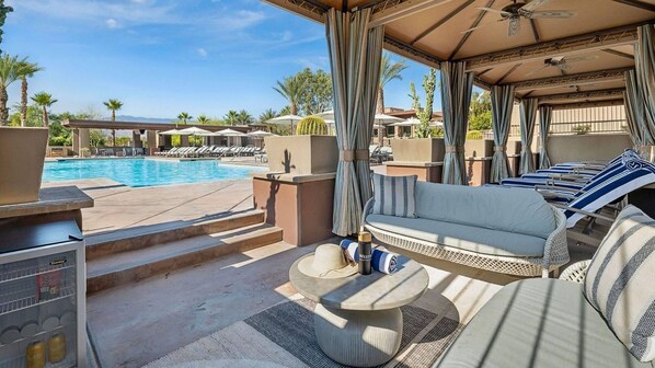 A poolside area with a sofa, umbrella, and a beverage cooler.