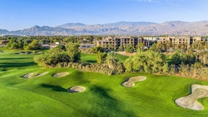 A golf course with bunkers and a building complex in the background.
