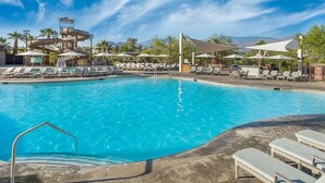 Piscina com espreguiçadeiras e guarda-sóis, um toboágua e vista para a montanha ao fundo.