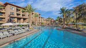 A hotel with a swimming pool, sun loungers, and palm trees.