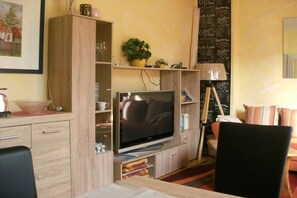 A living room with a flat-screen TV, wooden cabinets, a coffee-themed wall, and a dining area with a table and chairs. - Holiday apartment with 1 bedroom (Borkum)