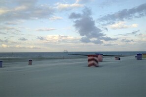 Ein Strand mit Sand, ein Schiff in der Ferne und gestreifte Strandsonnenschirme.