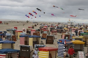 A beach with numerous beach huts, some with visible room numbers, and a variety of kites flying in the sky. - "To the Sunflower"||Borkum (Borkum)