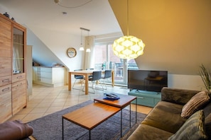 A modern living room with a sofa, a coffee table, a TV, and a dining area with chairs. - Holiday apartment with 3 bedrooms (Borkum)