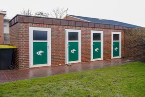 A row of four green doors with white numbers, each with a white animal symbol, on a brick building with a metal roof. - Holiday apartment with 3 bedrooms (Borkum)