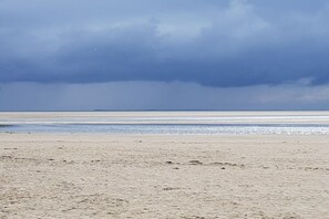Een strand met een breed zandstrand en een rustige zee onder een bewolkte lucht.