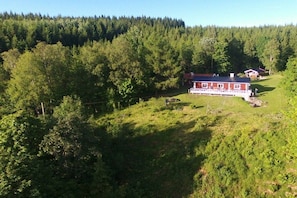 A red building with a white porch, surrounded by dense forest. - Holiday home with 2 bedrooms (Filipstad)