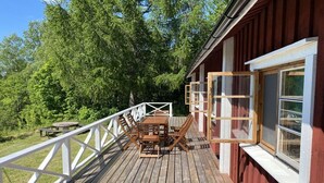 Eine Holzterrasse mit Tisch und Stühlen, umgeben von einem weißen Geländer, und ein rotes Gebäude mit Fenstern.