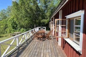 A wooden deck with a table and chairs, surrounded by a white railing, and a red building with windows. - Holiday home with 2 bedrooms (Filipstad)