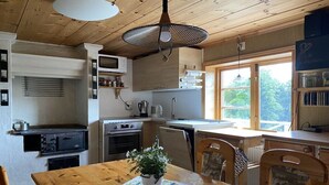 Eine Küche mit Holzschränken, einem Esstisch mit Stühlen, einer Hängelampe und einem Fenster, das für natürliches Licht sorgt.