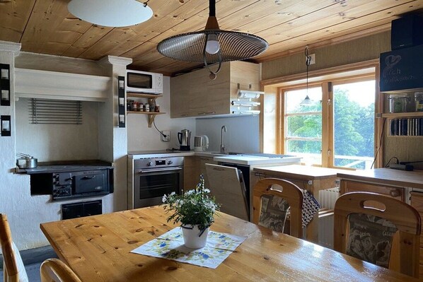 A kitchen with wooden cabinets, a dining table with chairs, a hanging light fixture, and a window providing natural light.