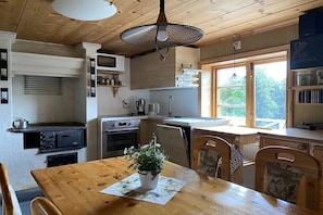 A kitchen with wooden cabinets, a dining table with chairs, a hanging light fixture, and a window providing natural light. - Holiday home with 2 bedrooms (Filipstad)