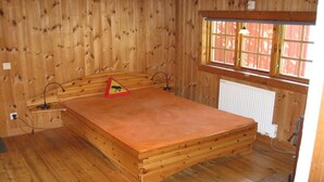 Ein Zimmer mit Holzwänden, einem Bett, einer Heizung und einem Fenster mit Blick.