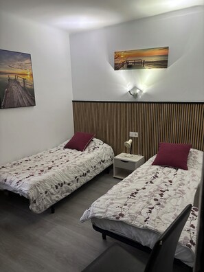 A bedroom with two single beds, a nightstand, a wall-mounted lamp, and a sunset painting. - Two-bedroom apartment near the ocean (roses)