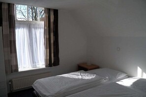 A room with a bed, a small wooden nightstand, a window with curtains, and a radiator. - ||--------------------House at Domburg----------------|| (Domburg)