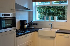 A kitchen with a stove, coffee maker, and a window with plants. - ||--------------------House at Domburg----------------|| (Domburg)