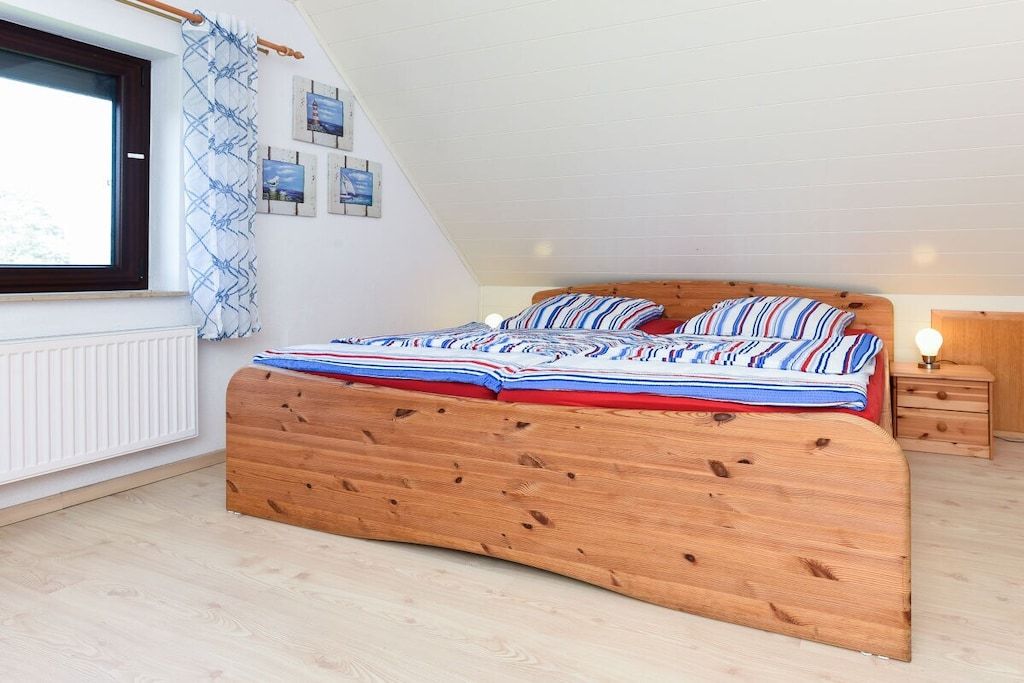 A bedroom with a wooden bed, a window with curtains, a bedside table with a lamp, and wall art.