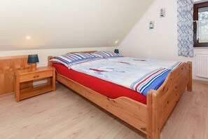 A single bed with a red mattress and striped bedding in a room with wooden flooring and a sloped ceiling. - Holiday home with 1 bedroom (Bensersiel)