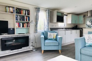 Ein Wohnzimmer mit Kamin, Bücherregal, Fernseher und blauem Sessel.