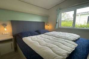 A bedroom with a bed, bedside lamps, and a window with curtains.