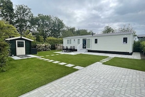 A mobile home with a small attached shed, a paved patio, and a well-maintained lawn.