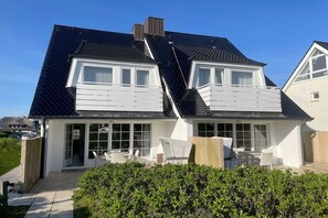 Ein zweistöckiges Haus mit einem geneigten Dach, großen Fenstern und einer Terrasse mit Gartenmöbeln.