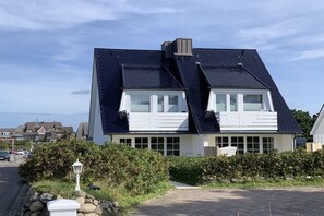 Ein zweistöckiges Haus mit geneigtem Dach, großen Fenstern und einem sichtbaren Schornstein.