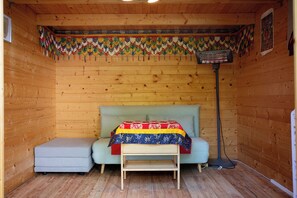 A wooden room with a bed, a bench, and a heater.