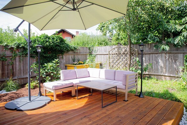A wooden deck with a beige umbrella, a white sofa, and a small table.