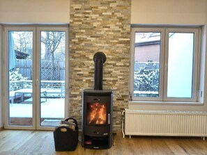 A room with a wood-burning stove, a stone wall, and large windows.