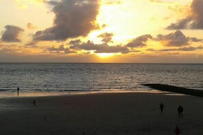 Ein Strand bei Sonnenuntergang, ruhige See und Menschen, die spazieren gehen.