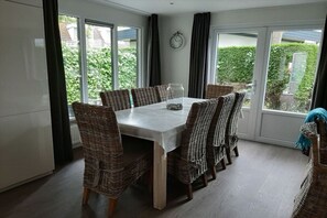 A dining area with a table and chairs, large windows, and a clock on the wall. - Holiday apartment in Zoutelande with Wi-Fi (Zoutelande)