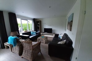 A living room with a sofa, a television, a coffee table, and a wicker chair. - Holiday apartment in Zoutelande with Wi-Fi (Zoutelande)