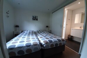 Une chambre avec deux lits, une table de chevet, une lampe et une salle de bain visible à travers une porte ouverte.