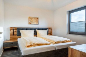 Ein Doppelbett mit Holz Kopfteil, ein Nachttisch, ein Fenster mit Jalousien.