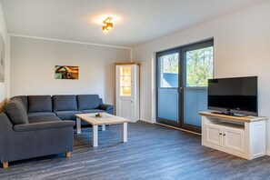 Ein modernes Wohnzimmer mit einem grauen Sofa, einem Couchtisch, einem Fernseher auf einem Holzboden und einem Schrank.