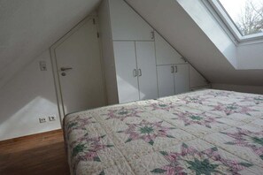 Ein Schlafzimmer mit schrägem Dach, einem Bett mit floraler Steppdecke und weißen Kleiderschränken.