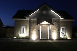 Uma casa residencial com fachada de pedra, telhado em duas águas e porta de entrada iluminada por iluminação externa.