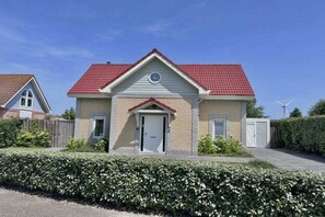 A two-story house with a red-tiled roof, a front door, and a small circular window above the door. - Holiday home with 4 bedrooms (Kamperland)