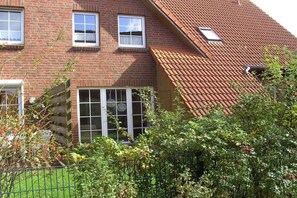Ein Backsteinhaus mit geneigtem Dach, einem sichtbaren Fenster und einem grünen Zaun.