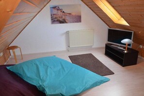 Une pièce avec un plafond en pente, un lit, une télévision, un radiateur et un tableau accroché au mur.