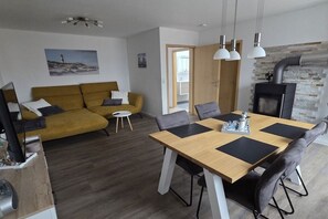 A modern living room with a sofa, a dining table with chairs, a fireplace, and a painting on the wall. - Holiday apartment with 2 bedrooms (Berumbur)
