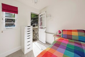 A bedroom with a bed, a dresser, a radiator, a window with a red blind, and a door leading outside. - Georgian Elegance in Islington, by Veeve (London)
