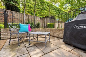 An outdoor patio with a metal table and chairs, a brick wall, and a covered grill area. - Georgian Elegance in Islington, by Veeve (London)