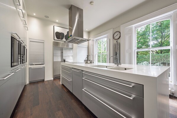 A modern kitchen with a large island, stainless steel appliances, and a view of greenery outside. - Georgian Elegance in Islington, by Veeve (London)