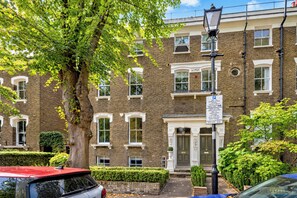 A multi-story brick building with a traditional facade, a large tree in the foreground, and a street lamp. - Georgian Elegance in Islington, by Veeve (London)
