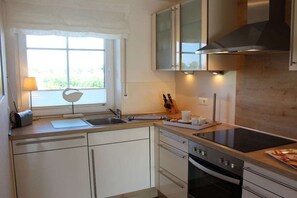 A kitchen with a window, a sink, a stove, and cabinets. - Holiday home with 2 bedrooms (Greetsiel)